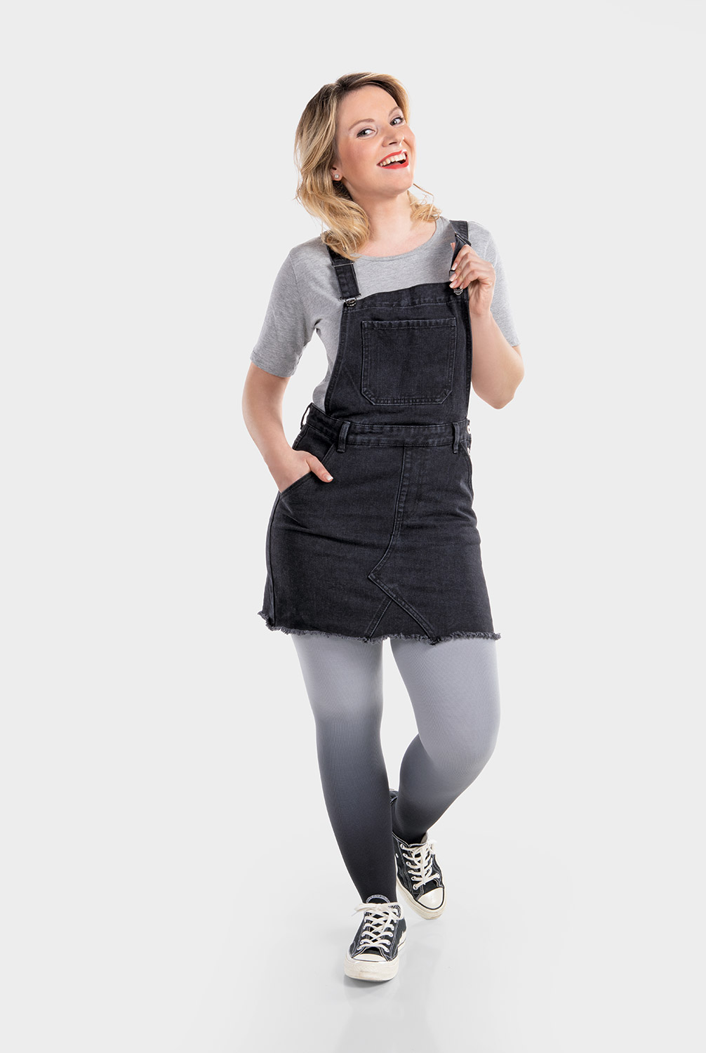 A woman is wearing a black pinafore dress and compression hosiery in dip-dye grey