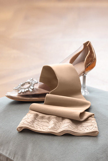 4. Lifestyle Bild Juzo Soft Juzo Soft Sesam liegt auf einem Kissen neben einem Cinderella Schuh
