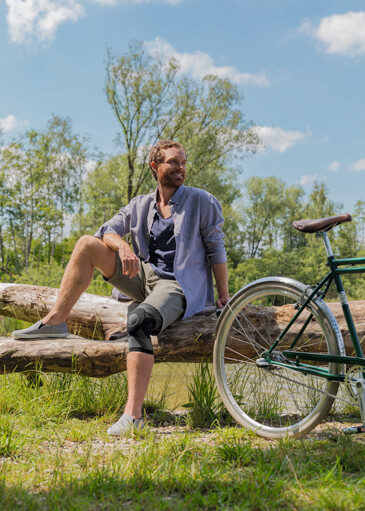 Juzo Flex Genu Xtra Ein Mann mit einer Kniebandage sitzt auf einem Baumstamm