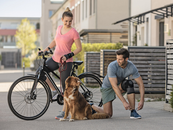 Eine Frau und ein Mann führen einen Hund Gassi mit einem Fahrrad