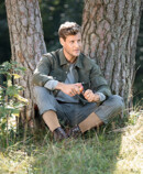 Man wearing Juzo Adventure, sitting under a tree and cutting an apple