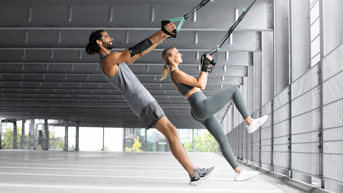 Un homme et une femme s'entraînent dans un parking souterrain avec une sangle TRX