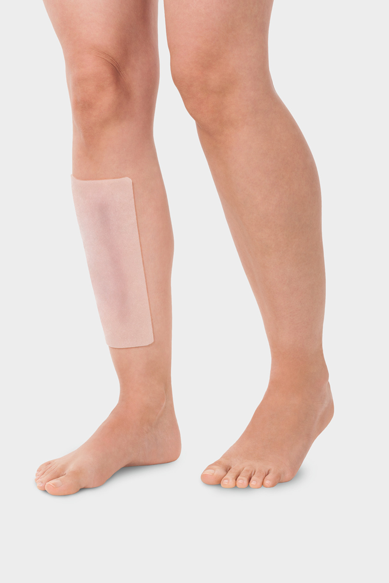 A person is wearing the Juzo ScarPad on their shin to treat a scar