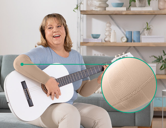 funktionszone albue Kvinde med Juzo Expert med funktionszone albue sidder på sofaen og spiller guitar