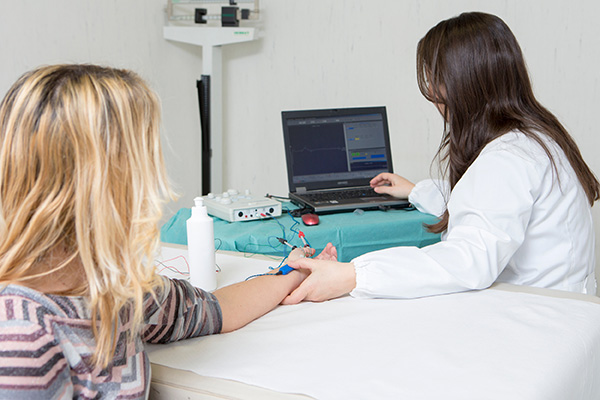 En læge udfører en elektroneurografi på en blond kvinde. Til dette formål er apparatet tilsluttet patientens arm.