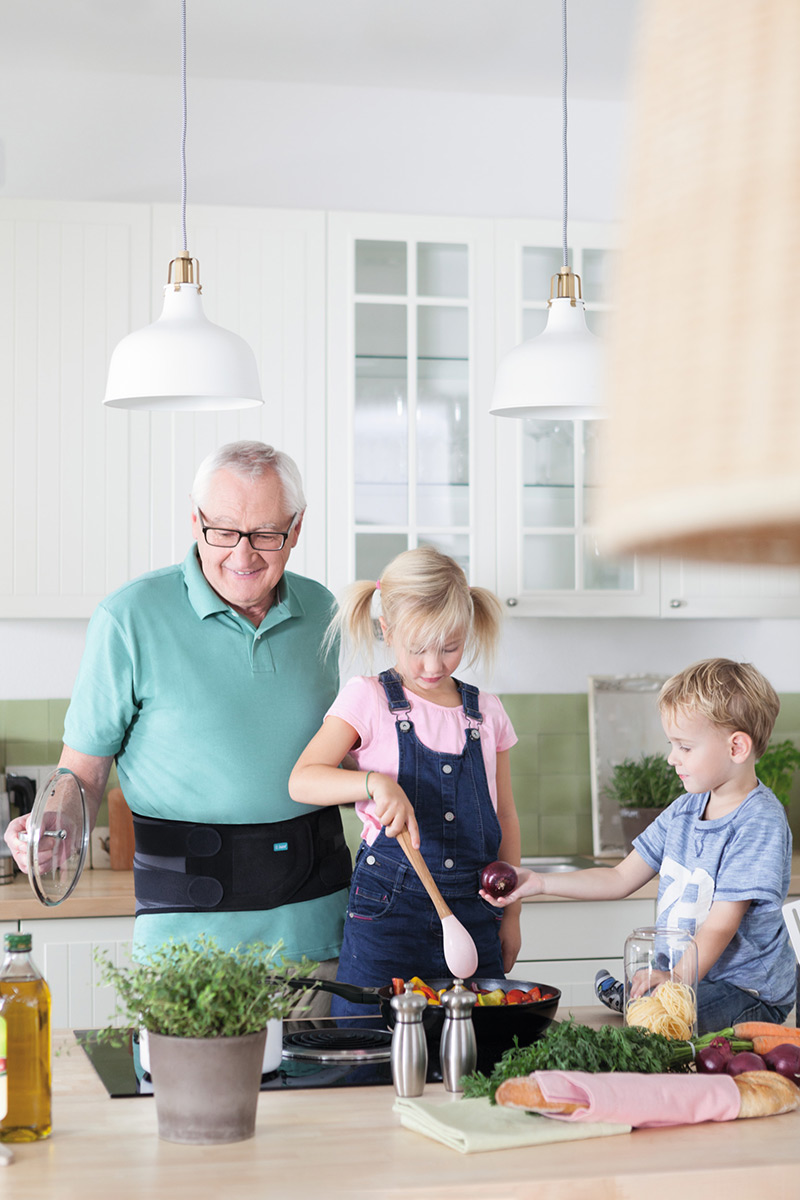Grandpa is cooking with his grandchildren. He is wearing a back orthosis. Grandpa is cooking with his grandchildren. He is wearing a back orthosis.