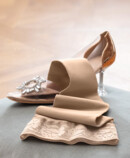 4. Lifestyle Bild Juzo Soft Juzo Soft Sesam liegt auf einem Kissen neben einem Cinderella Schuh